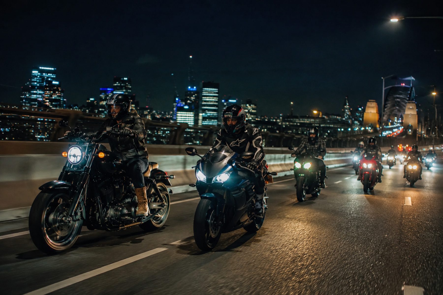 A pack of riders crossing a Sydney bridge at night, city lights behind them.